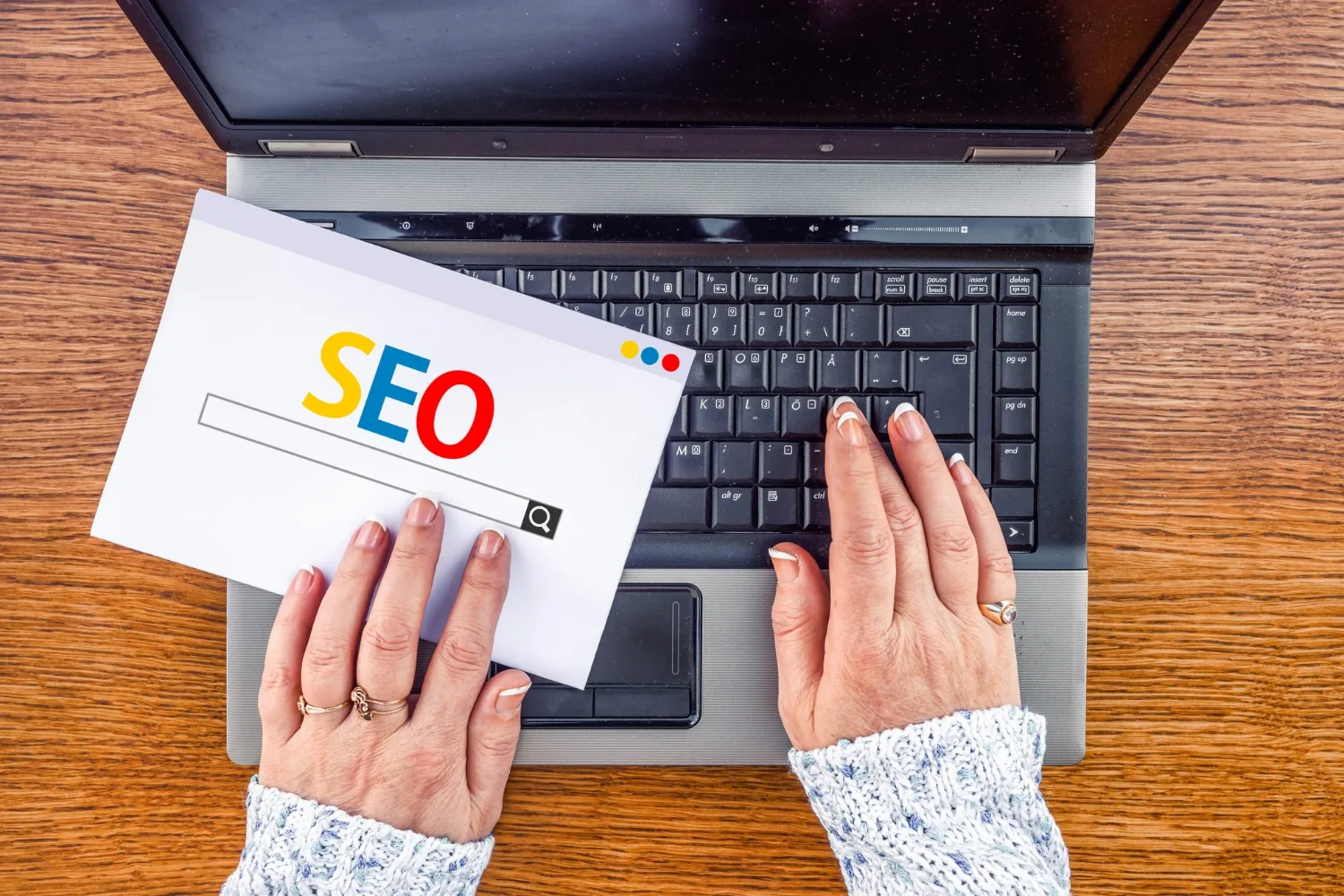 A hands using the laptop and a printed paper with SEO written on it