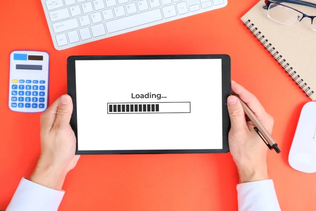 Hands holding a pen and tablet with a loading icon on the screen